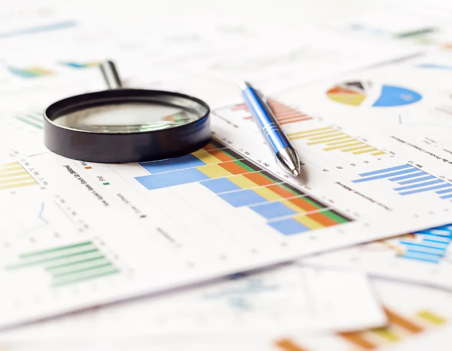 Documents d'analyse financière sur une table, avec loupe noire et stylo bleu