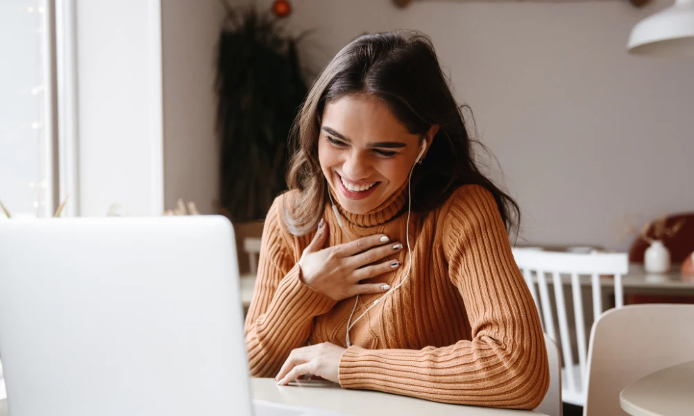 femme entrepreneure assise devant son portable. Elle a un grand sourire.