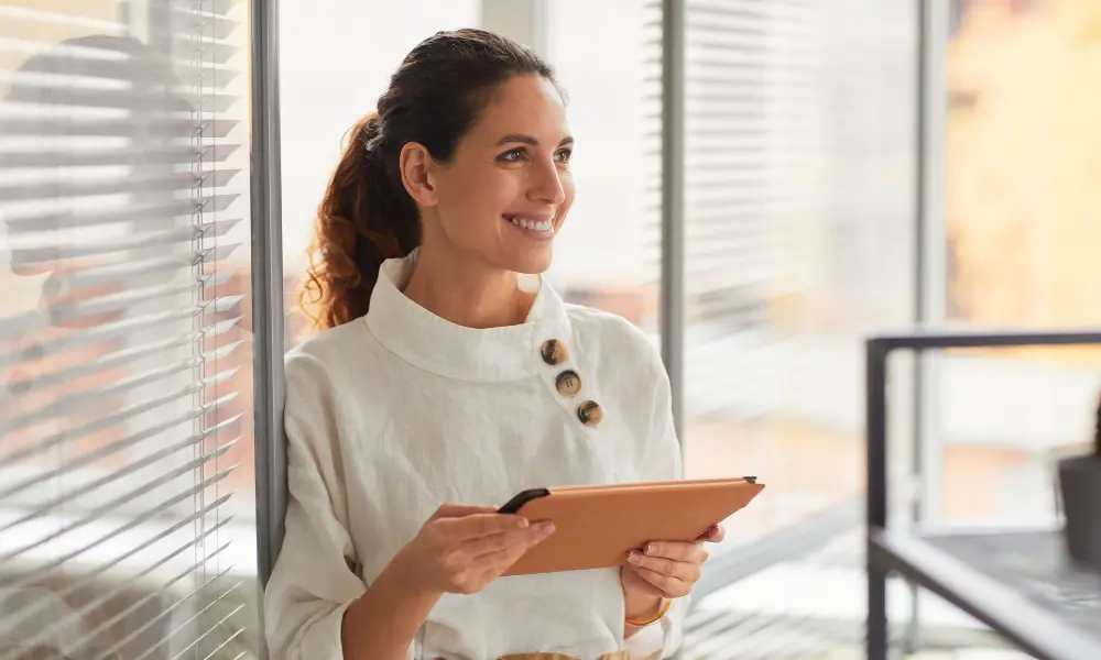 femme entrepreneure dans un bureau lumineux. Elle tient une tablette électronique dans un case orange.